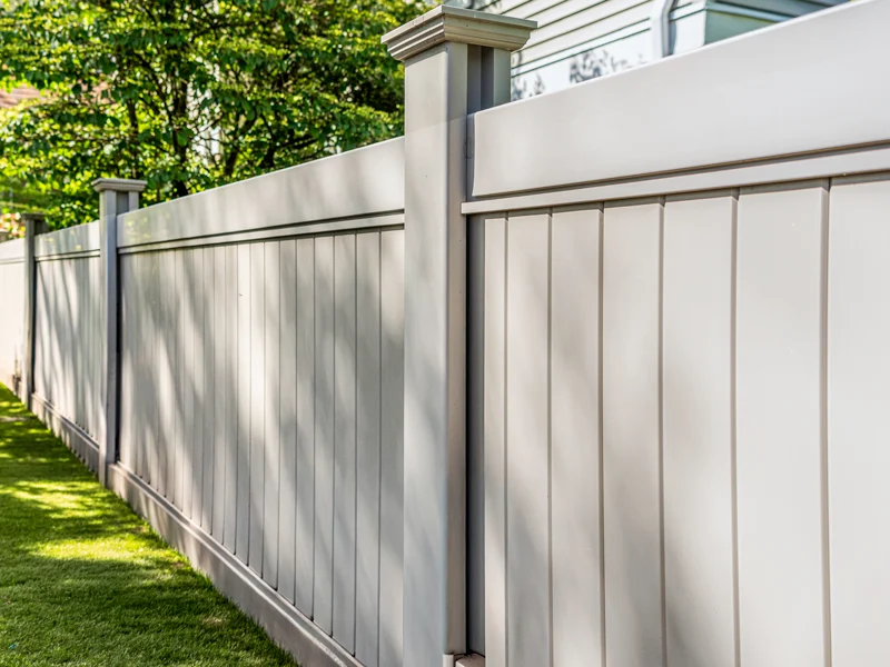 Long stretch of light gray vinyl fence with square posts along a grassy yard.